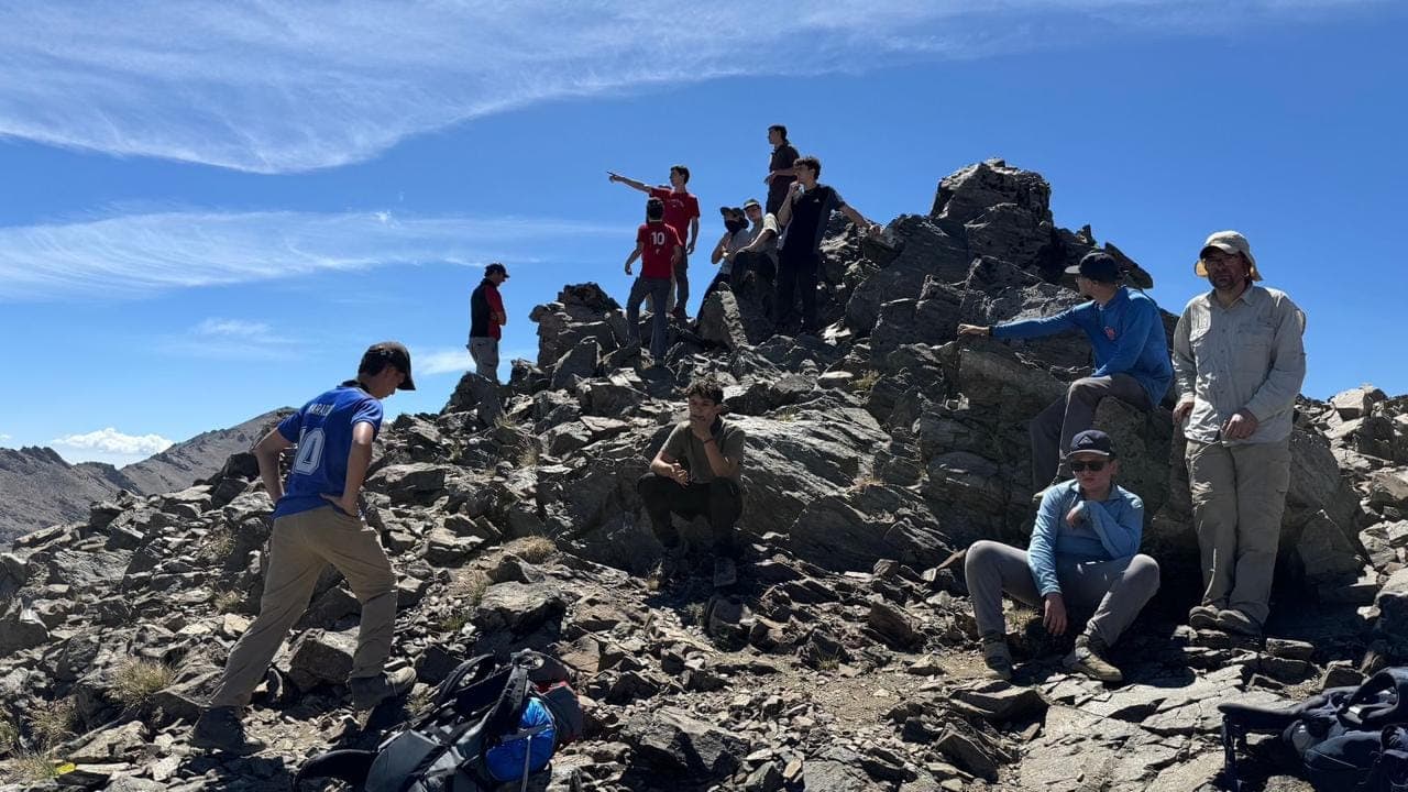 Chicos repartidos entre las rocas de una cumbre, con cielo despejado