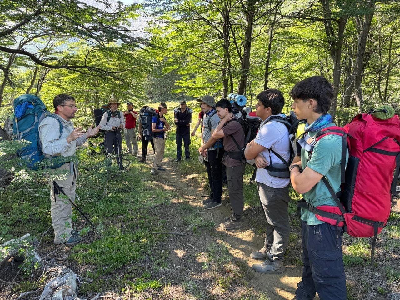 Un jefe de campamento hablándole al grupo en el bosque, todos con las mochilas puestas